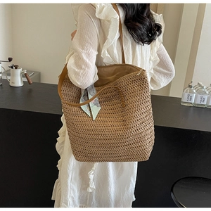 Detail of woven straw tote bag with brown straps and blue scarf on a summer dress