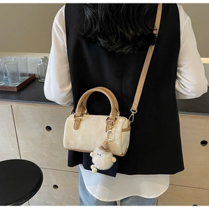 Close-up of beige Boston bag with brown handles and plush charm on a display shelf