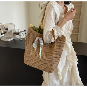 Close-up of the woven texture and leather strap on a large straw tote with a silk scarf
