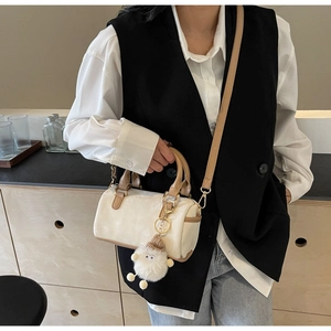 Detail of cream Boston bag with leather handles and a cute white plush lamb pendant