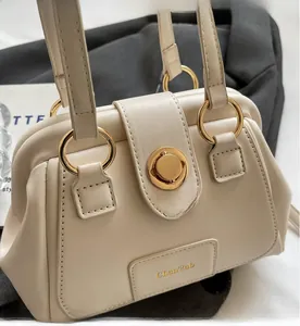 Detail of cream Boston bag with retro gold ring handle and metal rotary lock clasp