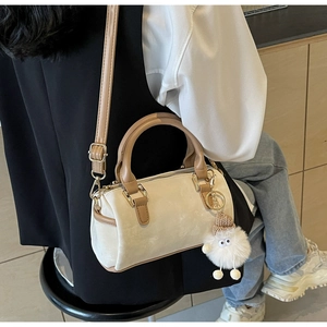 Detailed view of a cream Boston bag with brown handles and a cute plush charm accessory