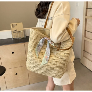 Detail of woven straw tote bag with brown leather handles and decorative silk scarf
