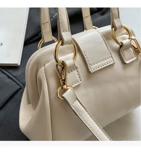 Close-up of cream beige Boston bag featuring polished gold metal handles and neat stitching