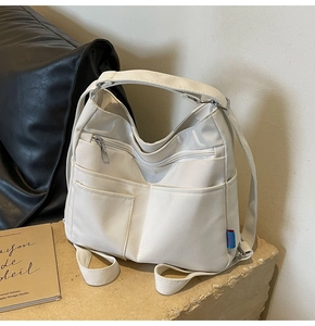Detail of cream multi-functional canvas shoulder bag with front zipper and side pockets
