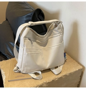 Detail of off-white canvas tote bag featuring multiple pockets and adjustable strap on stone