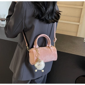 Pink velvet Boston bag with plush eye charm shown on a shoulder in a modern cafe