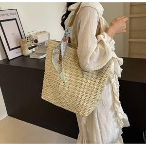 Detail of woven straw tote bag with brown leather straps and decorative scarf in cafe