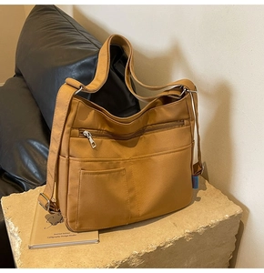 Detail of earthy brown nylon tote with multiple zipper pockets on stone surface