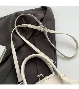 Detail of a creamy white handbags metal clasp and adjustable leather shoulder strap