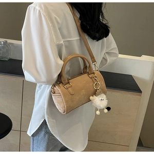 Side view of beige Boston bag with plush monster charm worn by model in white shirt