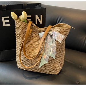 Close-up of woven straw tote bag with brown leather handles and a green floral silk scarf