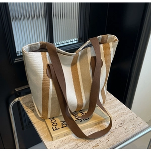 Detail of striped canvas tote bag with brown straps on a stone surface and books