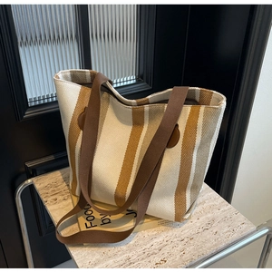 Detail view of large striped canvas tote bag with brown leather accents on marble surface