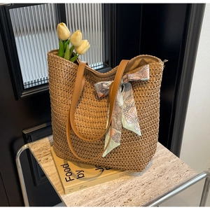Detail of woven straw tote bag with brown leather straps and colorful floral scarf decor