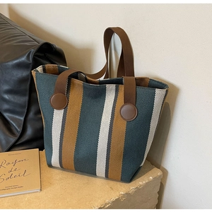 Detail of striped canvas tote bag with woven straps on a rustic stone base