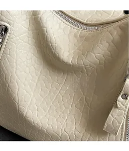 Vue macro de la texture cuir grainé blanc crème et détail zip argenté sur le sac cabas