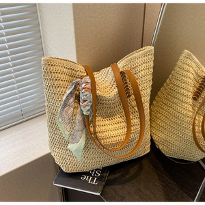 Detail of woven straw tote bag featuring brown leather straps and a floral silk scarf