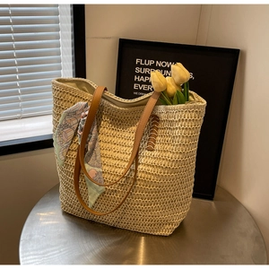 Detail of beige woven straw tote bag with brown leather handles and a floral silk scarf