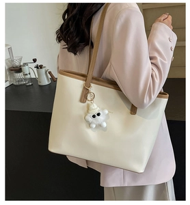 Detailed shoulder view of a large cream tote bag with brown straps and a cute plush charm