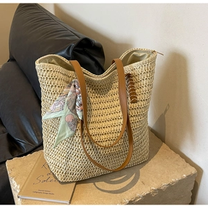 Detail of cream woven straw tote bag featuring brown faux leather straps and floral silk scarf