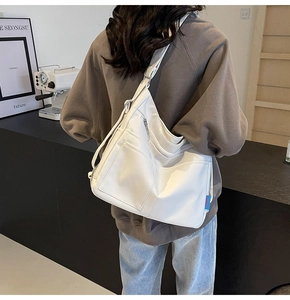 Detail of a large white tote bag featuring front zipper pockets and wide shoulder strap