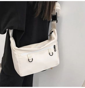 Close-up of off-white canvas crossbody tote featuring front zipper pocket and D-ring details