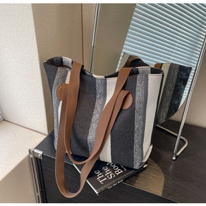 Detailed view of canvas tote bag with vertical stripes and brown leather strap accents