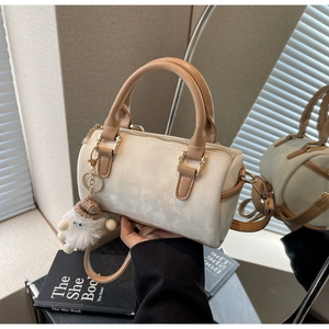 Close-up of cream Boston bag with leather handles and a plush monster charm detail