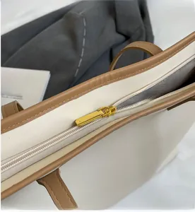 Detail of smooth gold zipper and brown leather trim on a minimalist tote bag