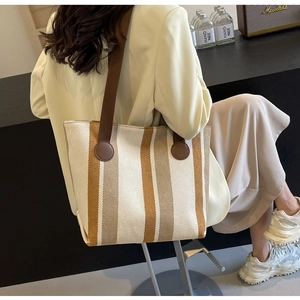Detail of canvas tote bag with brown vertical stripes and leather straps worn by model