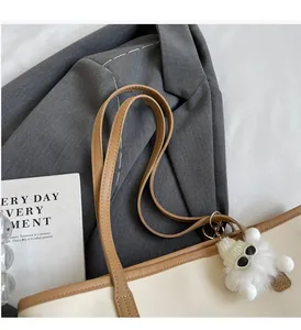 Detail of the cream tote bag handle and plush monster charm with a grey suit background