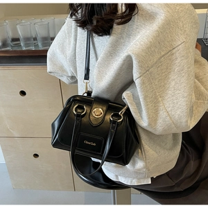Detail view of a black leather Boston bag with gold buckle and adjustable strap