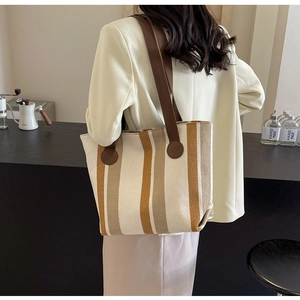 Detailed view of striped canvas tote bag with brown leather straps worn by a model
