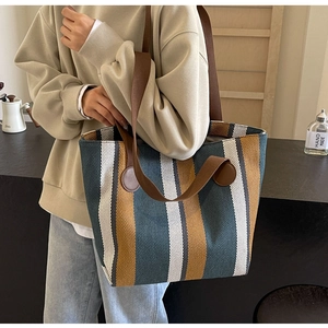Side view of large striped canvas tote bag with brown straps worn on shoulder
