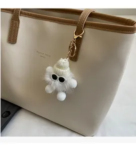 Detail of white fluffy faux fur pompom keychain with mini hat and sunglasses on a tote bag