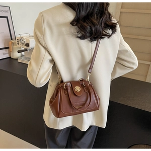 Brown leather Boston bag with gold twist lock shown in a lifestyle cafe setting