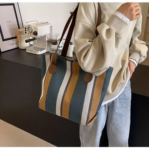 Detail view of canvas tote bag with vertical stripes and brown leather reinforcement
