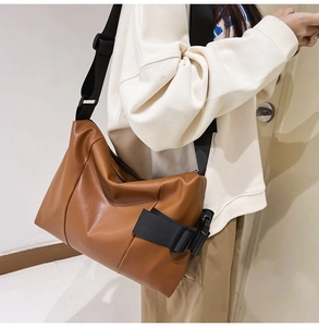 Brown PU leather tote bag with wide black nylon strap worn as a crossbody messenger