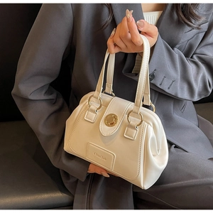 Close-up of cream Boston bag with gold circular metal handles and logo engraving