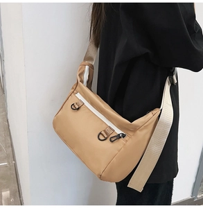 Detail of khaki nylon tote bag showing white zippers and functional D-ring attachment