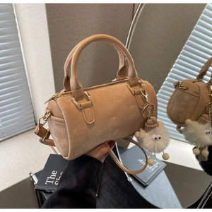 Detail of beige suede boston bag with twin handles and a plush lamb pendant charm