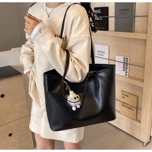 Close-up of black leather tote bag with a white plush ghost charm on a wooden background
