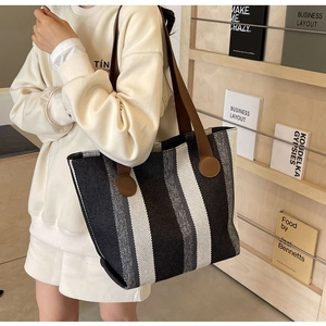 Detail of striped canvas tote bag showing wide brown straps and reinforced patches