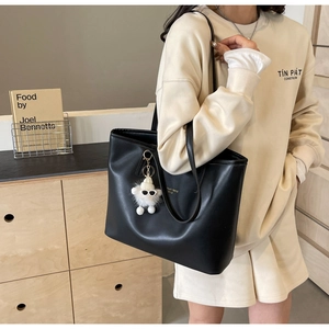Detailed view of a black tote bag with white plush charm worn on a shoulder