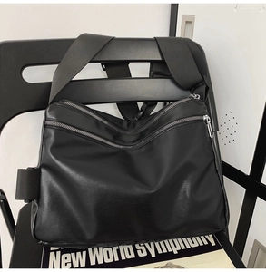 Detail of black PU tote bag showing double silver zippers and wide nylon shoulder strap
