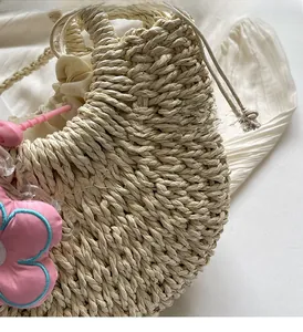 Macro detail of hand-woven straw bag with beige drawstring lining and pink flower charm
