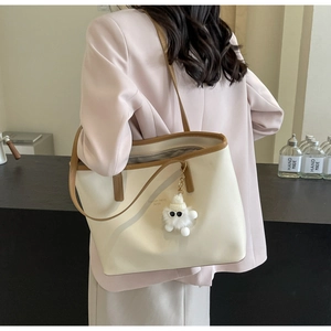 Lifestyle view of large beige tote bag with brown straps and plush charm on shoulder