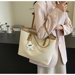 Detail of off-white tote bag with brown trim, long straps and cute monster charm accessory