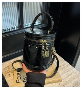 Detail of black quilted bucket bag with gold lock charm and glossy leather finish
